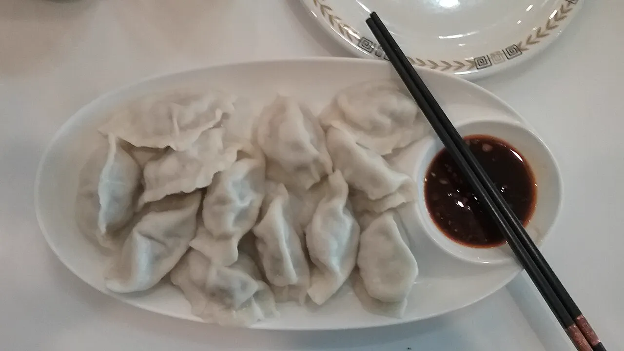 A plate of boiled pork and cabbage jiaozi dumplings with dipping sauce